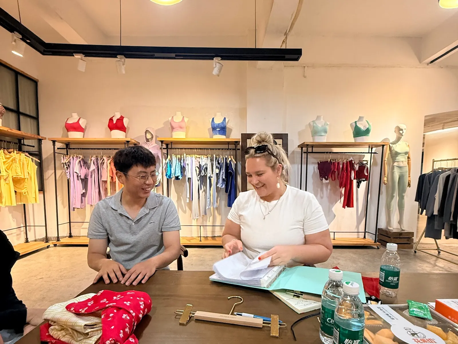 Reviewing design documents and product samples with a supplier at a table in a clothing sample showroom
